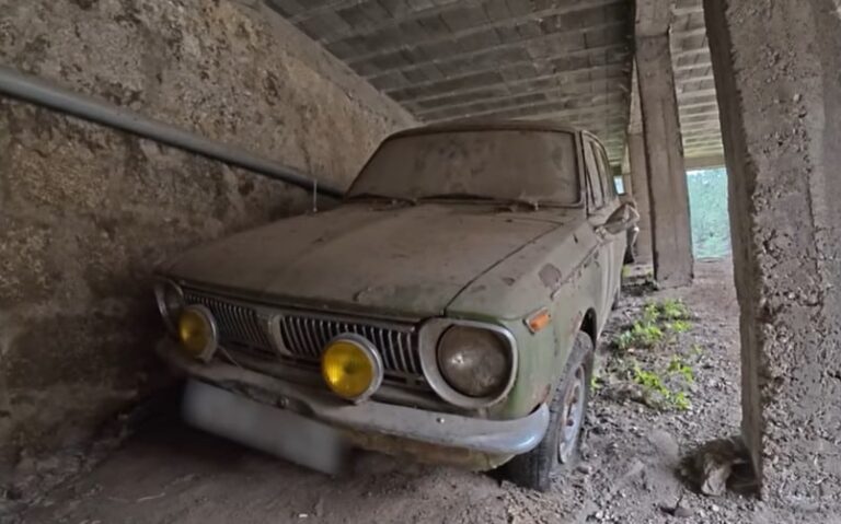 Interior de un galpón abandonado con varios autos clásicos japoneses de los años 70 cubiertos de polvo.