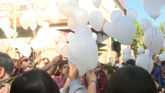 Personas reunidas frente a una escuela en Merlo, soltando globos y con velas encendidas en un homenaje.