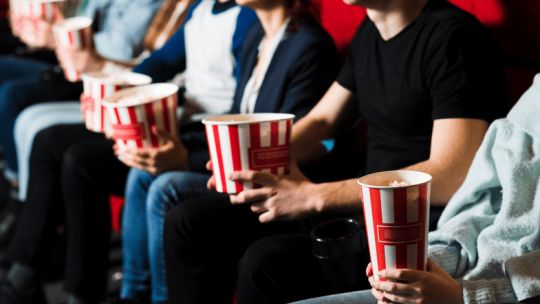 Personas comprando entradas de cine online con un teléfono móvil, mostrando la promoción de BBVA y Cinemark.