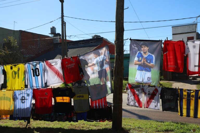 Remeras de fútbol colgadas al sol en un puesto callejero de Moreno, con la imagen de Diego Maradona